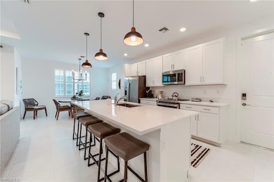 Kitchen with stainless steel appliances, a sink, a kitchen bar, white cabinetry, and a kitchen island with sink