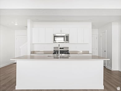 Kitchen with white cabinets, dark wood finished floors, appliances with stainless steel finishes, a center island with sink, and light stone counters