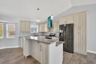 Kitchen featuring cream cabinets, light stone counters, appliances with stainless steel finishes, backsplash, and hanging light fixtures