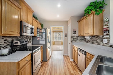 Kitchen featuring tasteful backsplash, stainless steel appliances, light wood-type flooring, light countertops, and recessed lighting