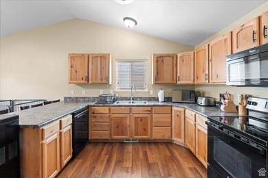 Kitchen featuring black appliances, dark countertops, dark wood-type flooring, a peninsula, and vaulted ceiling