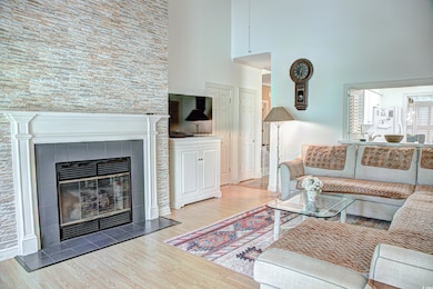 Living area with light wood-style flooring, a tiled fireplace, and a high ceiling