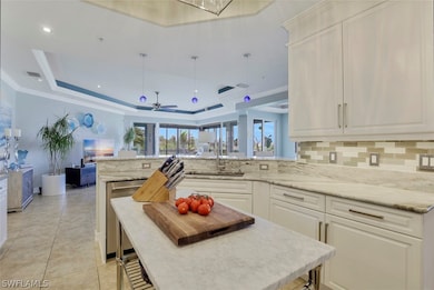 Kitchen featuring white cabinets, light stone counters, ceiling fan, and a raised ceiling