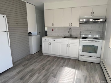 Kitchen featuring white appliances, a baseboard radiator, washer / dryer, white cabinets, and under cabinet range hood