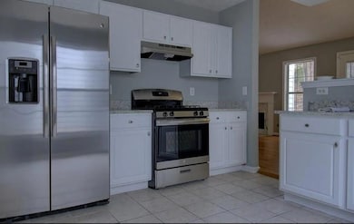 Kitchen featuring appliances with stainless steel finishes, under cabinet range hood, white cabinets, light stone counters, and light tile patterned flooring