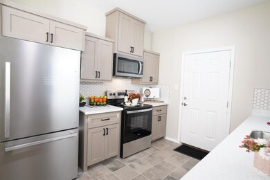 Kitchen with appliances with stainless steel finishes, decorative backsplash, gray cabinetry, and light stone counters