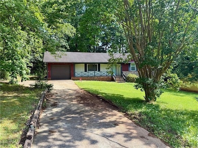 Ranch-style house with concrete driveway, an attached garage, a front yard, and covered porch