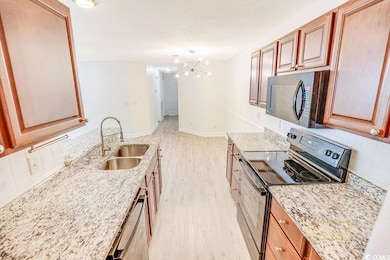 Kitchen featuring appliances with stainless steel finishes, light wood-style flooring, tasteful backsplash, a chandelier, and light stone counters