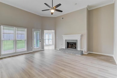 Unfurnished living room featuring light wood-style floors, crown molding, a brick fireplace, a ceiling fan, and a towering ceiling