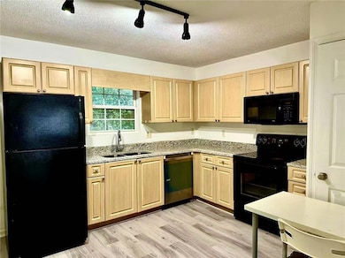 Kitchen featuring light brown cabinetry, black appliances, a textured ceiling, light wood-type flooring, and track lighting