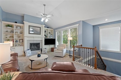 Carpeted living room featuring lofted ceiling, a tiled fireplace, and ceiling fan