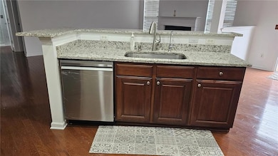 Kitchen with dark wood finished floors, light stone countertops, and an island with sink