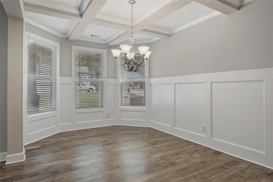 Unfurnished dining area with a decorative wall, beamed ceiling, a chandelier, coffered ceiling, and a wainscoted wall