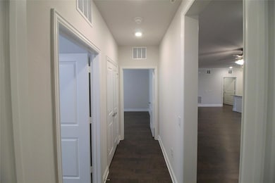 Corridor with dark wood-style floors, visible vent
