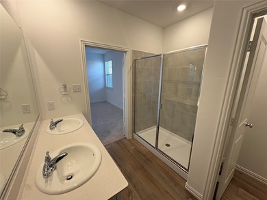 Full bath with dark wood-style flooring, double vanity, and a shower stall