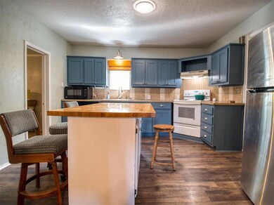 Kitchen featuring butcher block countertops, electric stove, freestanding refrigerator, blue cabinetry, and black microwave