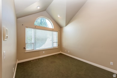 Spare room featuring dark carpet and vaulted ceiling