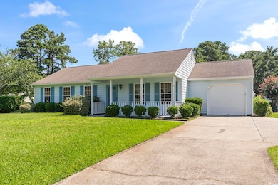 View of front of house featuring covered porch, driveway, roof with shingles, a garage, and a front lawn