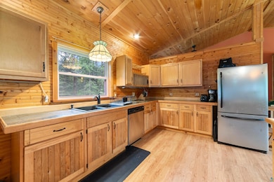 Kitchen featuring appliances with stainless steel finishes, light brown cabinetry, light wood finished floors, wooden walls, and hanging light fixtures