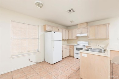 Kitchen with light tile patterned flooring, white appliances, light brown cabinets, light countertops, and a peninsula
