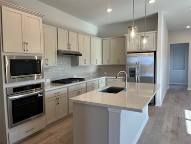 Kitchen featuring tasteful backsplash, stainless steel appliances, light wood-type flooring, decorative light fixtures, and light stone counters