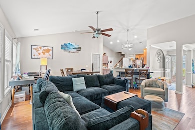 Living room with vaulted ceiling, a ceiling fan, light wood finished floors, stairway, and baseboards