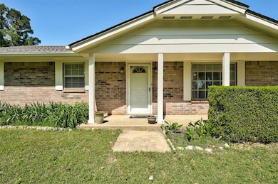 Property entrance with brick siding, a porch, a yard, and a shingled roof