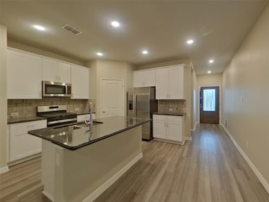 Kitchen with decorative backsplash, appliances with stainless steel finishes, white cabinetry, recessed lighting, and dark stone countertops