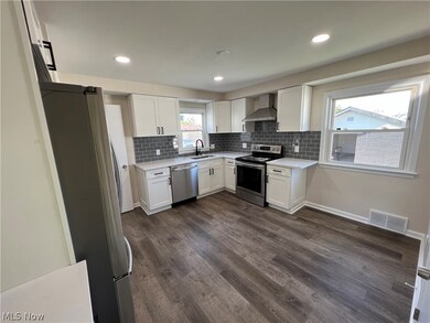 Kitchen with wall chimney exhaust hood, white cabinetry, stainless steel appliances, and dark hardwood / wood-style floors