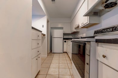 Kitchen featuring white fridge, light tile patterned floors, white cabinets, range with electric cooktop, and extractor fan
