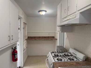 Kitchen with white range with gas stovetop, white cabinets, under cabinet range hood, tasteful backsplash, and dark countertops