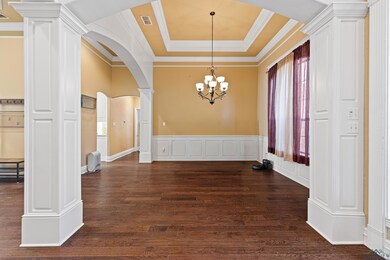 Unfurnished dining area featuring ornate columns, arched walkways, a raised ceiling, crown molding, and dark wood finished floors