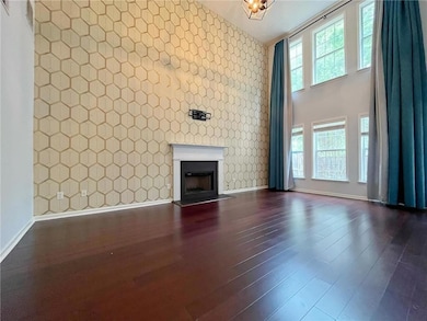 Unfurnished living room featuring dark wood-style flooring, baseboards, wallpapered walls, a high ceiling, and an accent wall