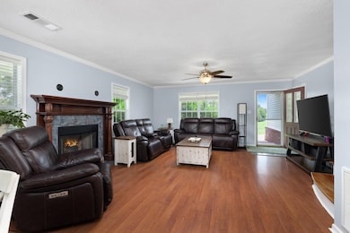 Living room with wood finished floors, a fireplace, a textured ceiling, a ceiling fan, and healthy amount of natural light