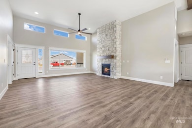 Unfurnished living room with a high ceiling, a ceiling fan, wood finished floors, a stone fireplace, and recessed lighting