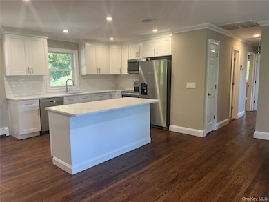 Kitchen with appliances with stainless steel finishes, white cabinets, ornamental molding, recessed lighting, and a kitchen island