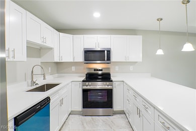 Kitchen featuring stainless steel appliances, white cabinetry, hanging light fixtures, and light stone countertops