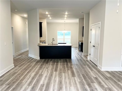Kitchen with dark cabinets, a peninsula, hanging light fixtures, light stone countertops, and light wood-style flooring