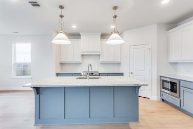Kitchen featuring white cabinetry, black microwave, sink, and an island with sink