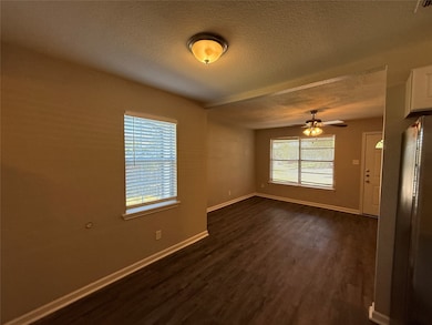Empty room with a textured ceiling, dark wood-type flooring, and ceiling fan