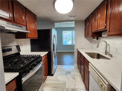 Kitchen with stainless steel gas range oven, white dishwasher, under cabinet range hood, light marble finish floors, and decorative backsplash