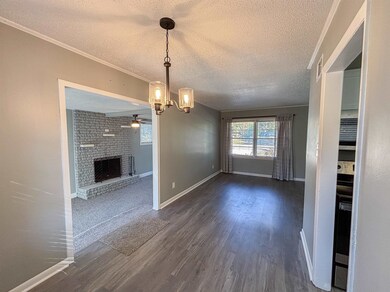 Unfurnished dining area featuring a textured ceiling, a fireplace, dark wood-style flooring, a ceiling fan, and a chandelier