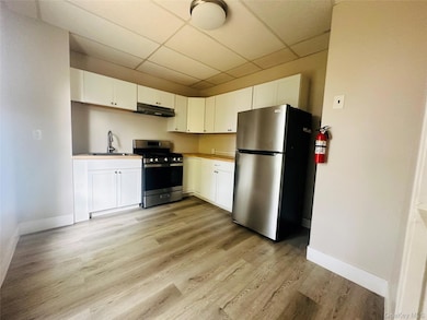 Kitchen featuring appliances with stainless steel finishes, a paneled ceiling, white cabinets, light countertops, and light wood finished floors