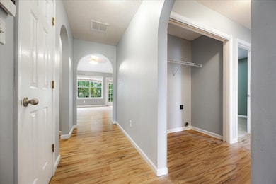 Corridor with arched walkways, light wood-style floors, baseboards, and a textured ceiling