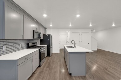 Kitchen featuring gray cabinets, stainless steel appliances, an island with sink, decorative backsplash, and light wood-style floors
