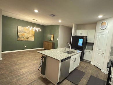 Kitchen featuring light stone counters, black appliances, white cabinetry, an island with sink, and recessed lighting