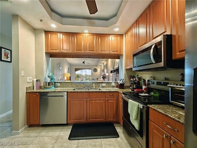 Kitchen featuring ceiling fan, appliances with stainless steel finishes, recessed lighting, a tray ceiling, and stone counters