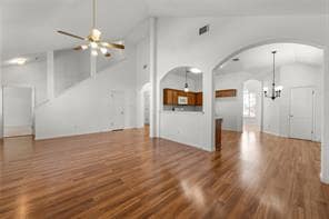 Unfurnished living room featuring arched walkways, dark wood finished floors, a chandelier, high vaulted ceiling, and ceiling fan