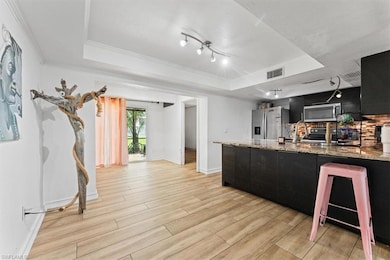 Kitchen with stainless steel appliances, track lighting, light wood-type flooring, ornamental molding, and a tray ceiling