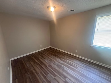 Unfurnished room featuring dark wood-style flooring, a textured ceiling, and baseboards